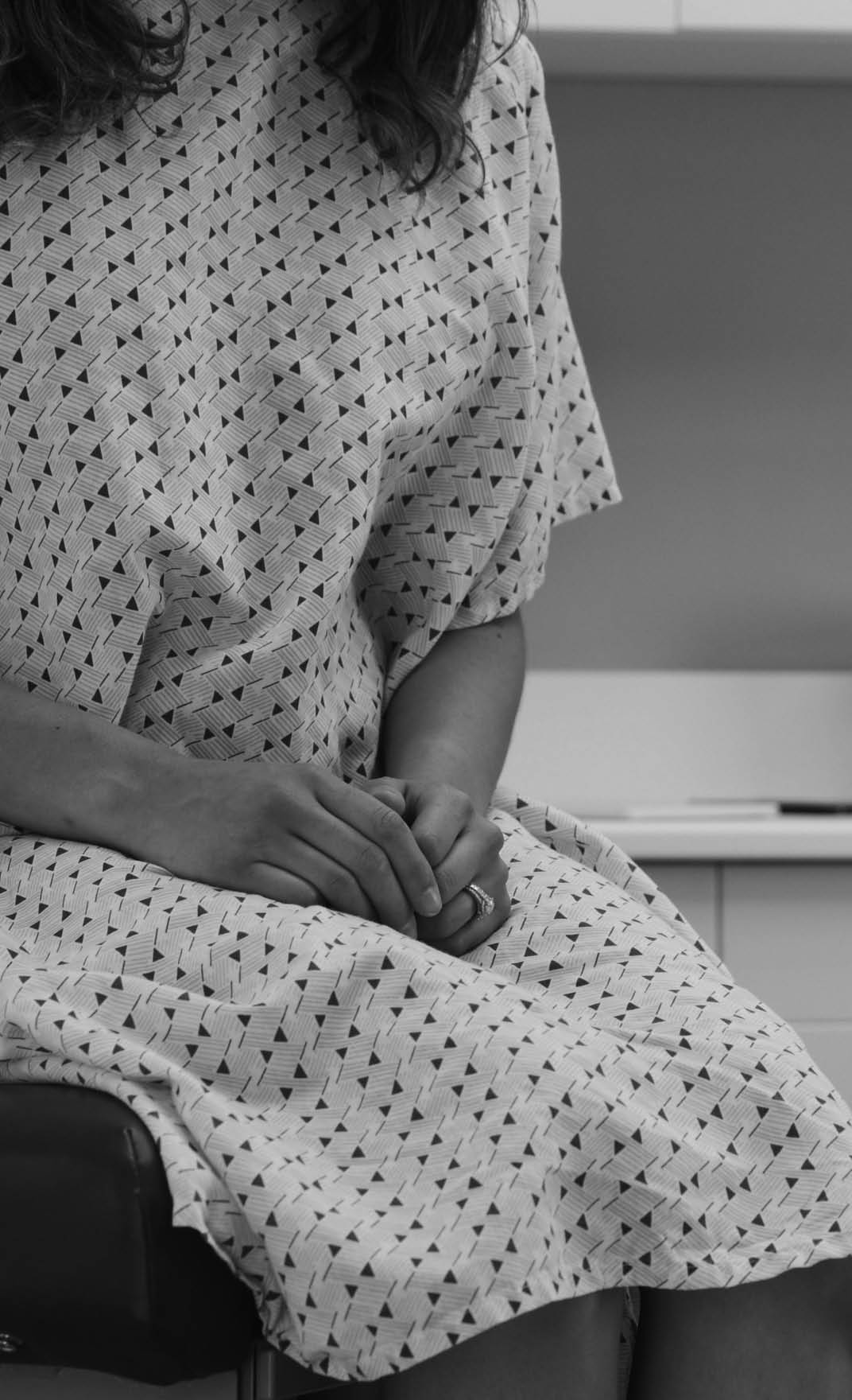 Portrait of young female patient seated on clinic chair wearing hospital gown